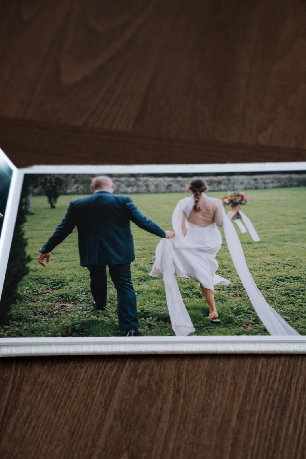 Fotografía impresa de una boda: los novios caminando de espaldas sobre la hierba, apoyada en una mesa de madera