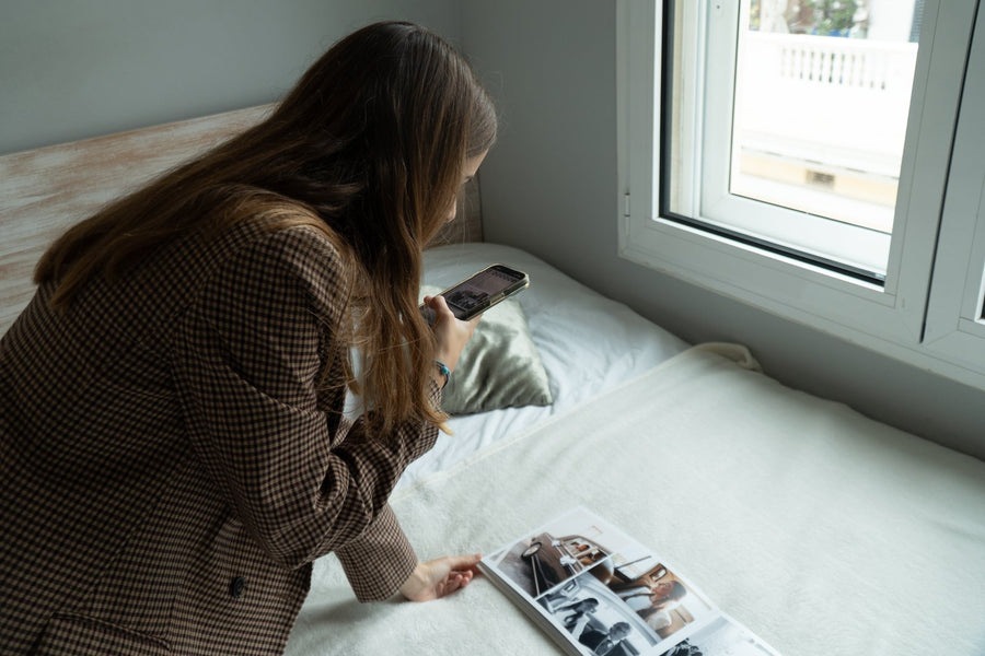 Una chica mira una foto de boda en el móvil junto a un álbum de boda abierto sobre la cama