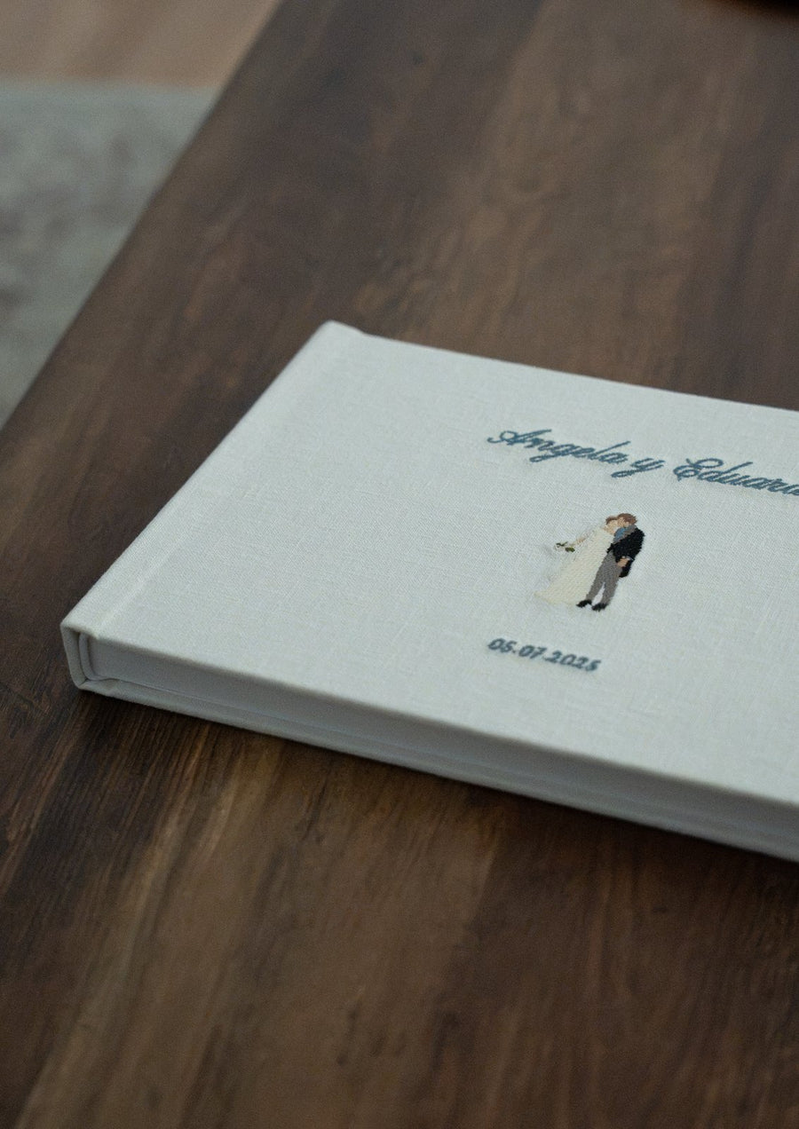 Álbum de boda de lino con los nombres de la pareja y la fecha bordados a mano, sobre una mesa de madera