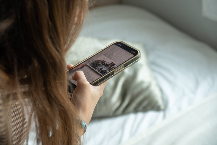 Una chica mira en el móvil la foto de un álbum de boda abierto, sentada junto a una cama